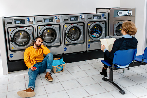 People in the laundromat. Man using mobile phone