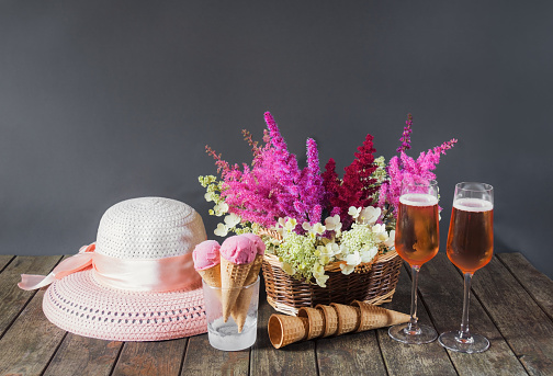 Beautiful astilbe and hydrangea flowers, glasses of rose champagne, summer hat, cherry ice cream and waffle cones on wooden table. Selective focus. View with copy space.