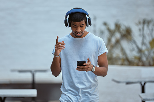 Shot of a young man using a smartphone and headphones against an urban background