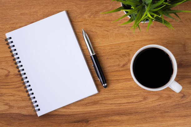 istock Top view of open school notebook with blank pages, coffee cup and pen for taking write notes on wood table background. Flat lay, creative workspace office. Business-education concept with copy space. 1299762480