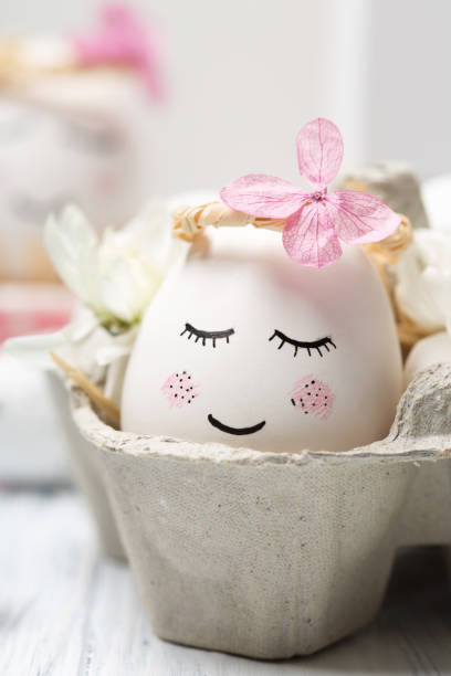 istock Easter holiday concept with cute handmade white eggs, tree branches, quail feathers and spring flowers on white wooden background. 1299763441