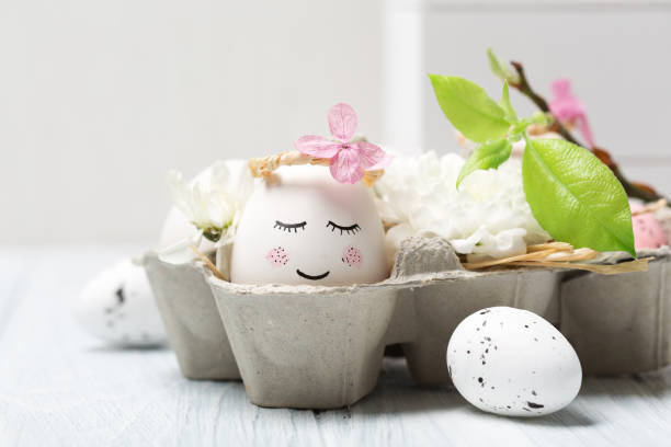 istock Easter holiday concept with cute handmade white eggs, tree branches, quail feathers and spring flowers on white wooden background. 1299763448