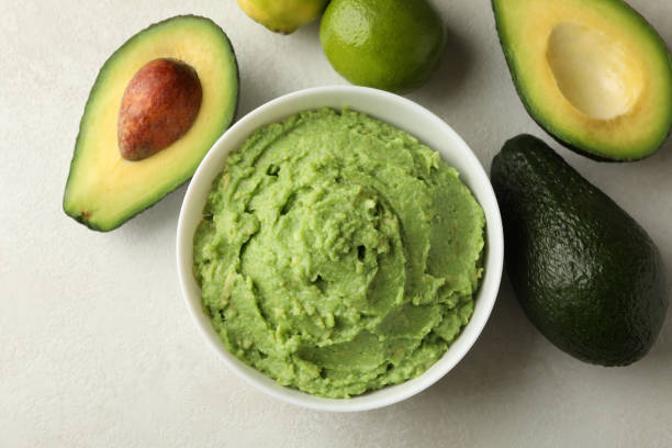 istock Bowl of guacamole, avocado and lime on white textured background, top view 1299764519