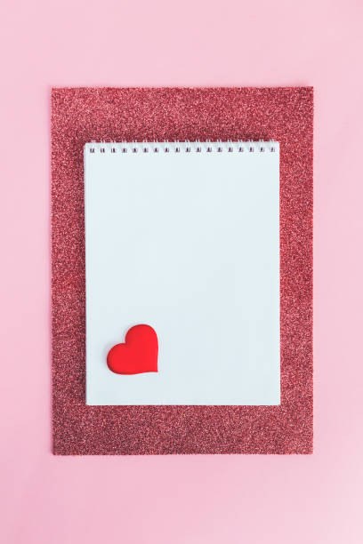 istock Notebook with blank page and red heart on a pink glitter background. 1299764697