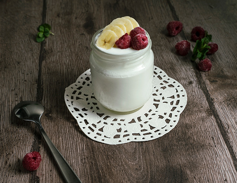 Natural homemade yoghurt in a glass jar with banana slices and raspberries. Healthy breakfast with Greek yogurt