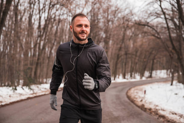 istock Man wearing jacket and gloves jogging while listening music 1299766672