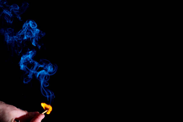 istock Blue curly smoke from a lit match in a holding hand isolated on a black background. Abstract mystical smoke 1299767483