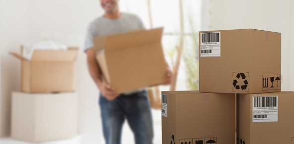 Graphic 3D image of cardboard courier boxes against smiling man carrying boxes in new house