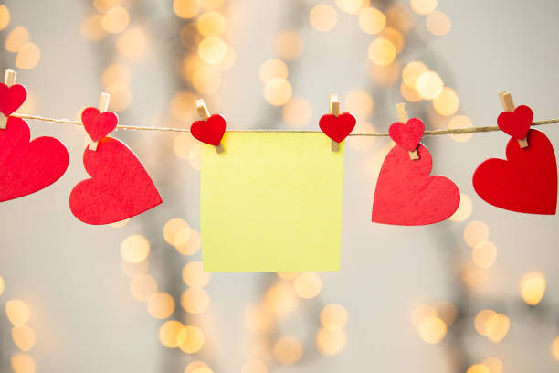istock Blank Yellow sticky note hanging with red hearts with bokeh background, romantic Valentines day concept background copy space 1299769169