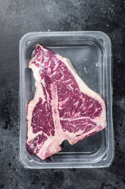 istock T-bon raw beef steak in vacuum packaging. Black background. Top view 1299769815