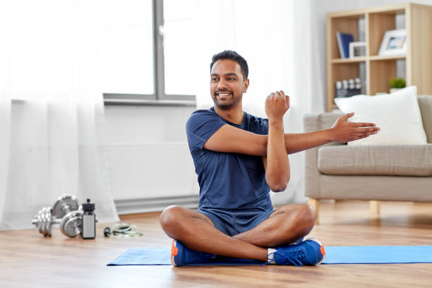 man training and stretching arm at home sport, fitness and healthy lifestyle concept - indian man training and stretching arm at home home workout stock pictures, royalty-free photos & images