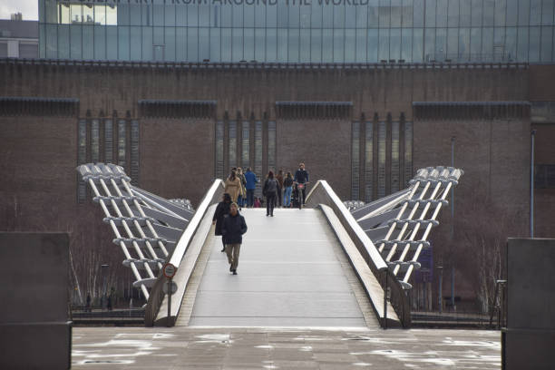 London, United Kingdom - January 29 2021: People walking on Millennium Bridge and Tate Modern exterior, daytime view.