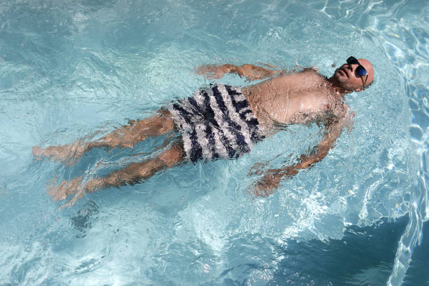 istock Young bald handsome man floating in a swimming pool wearing sunglasses 1299770880