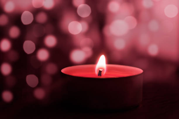 One candle of pink color close-up on the background of bokeh, glow. The image is designed in pink tones