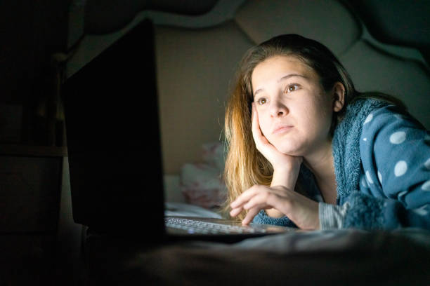 istock Young woman reading messages on laptop relaxing in bed 1299773572