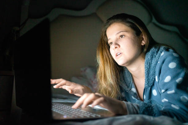 istock Young woman reading messages on laptop relaxing in bed 1299775027