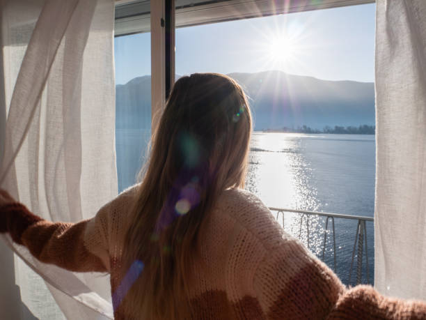 Female opens curtains at sunrise, new beginning new day Young woman standing on her balcony taking a breath of fresh air in the morning hotel window view stock pictures, royalty-free photos & images