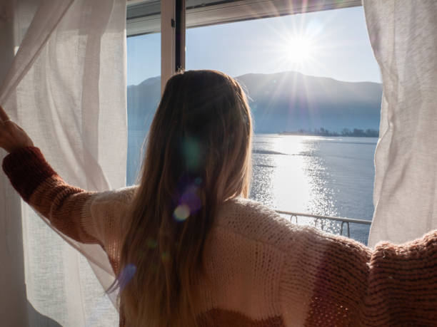 istock Female opens curtains in the morning, lake view 1299775526
