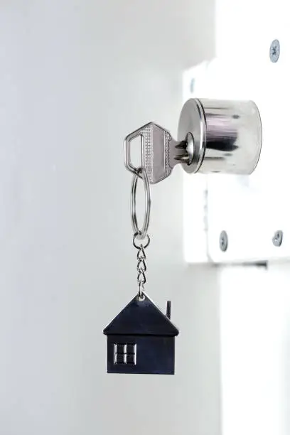 Silver house key in white door, with little keychain house, opening door to new house, home, investment, real estate concept, space for text close up