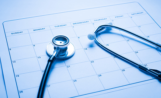 Appointment with a doctor concept. Close up photo of paper blank calendar with medical tool stethoscope on practitioner's tabletop