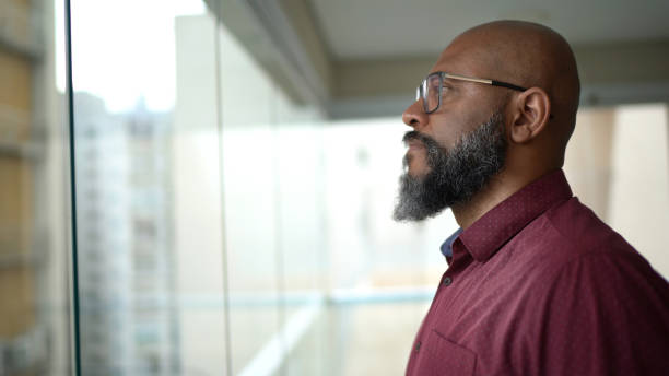 istock Mature man looking through the window at home 1299778011