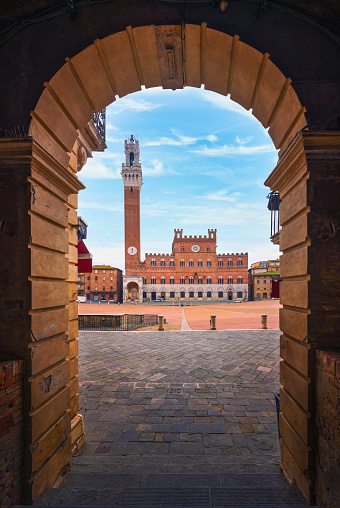 Siena, Piazza del Campo square, Torre del Mangia tower and Palazzo Pubblico building. Arch as a frame. Tuscany, Italy.