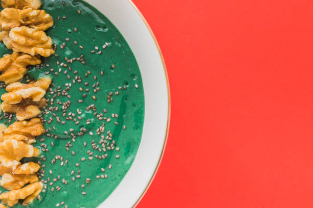 spirulina smoothie bowl with banana, walnuts, kiwi and chia seeds on red background