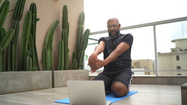 Mature man exercising at home while watching online class Mature man exercising at home while watching online class exercise class photos stock pictures, royalty-free photos & images