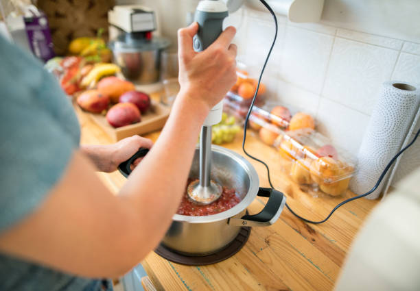 Woman standing in her kitchen using a stick blender to make sauce stock photo