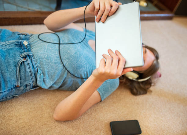 istock Young woman using a tablet while lying on her living room floor 1299781037