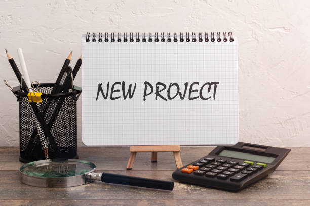 istock Text NEW PROJECT on white card lying on notepad on office desk. Business concept. 1299783934