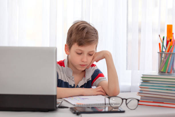 istock Portrait kid sitting at the table on computer, studying in home. Tired schoolboy with a pile of books and notebook. 1299784508