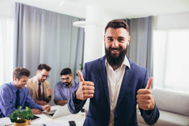 istock Businessman looking at camera posing in office with diverse happy team at background. 1299784880