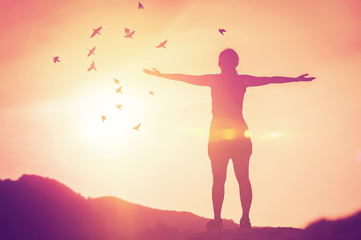 Freedom feel good and travel adventure concept. Copy space of silhouette woman rising hands on sunset sky at top of mountain and bird fly abstract background. Vintage tone filter effect color style.