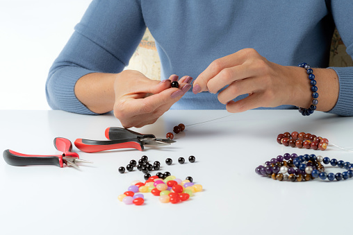 Jewelry making. Production bracelets and necklaces from multi-colored beads. Female hands with a tool on a white. Selective focus.