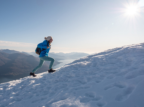 Woman hiker walking uphill on snowy mountain ridge. Sportive young female on a hike ascending mountain in winter. Relentless achievement concept