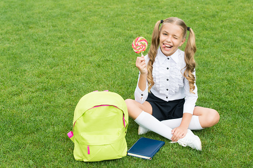 small girl hold book. lollipop for kid. childhood developing. girl with notebook and candy. back to school. kid with school bag. smiling child with backpack. sweet teen youth.