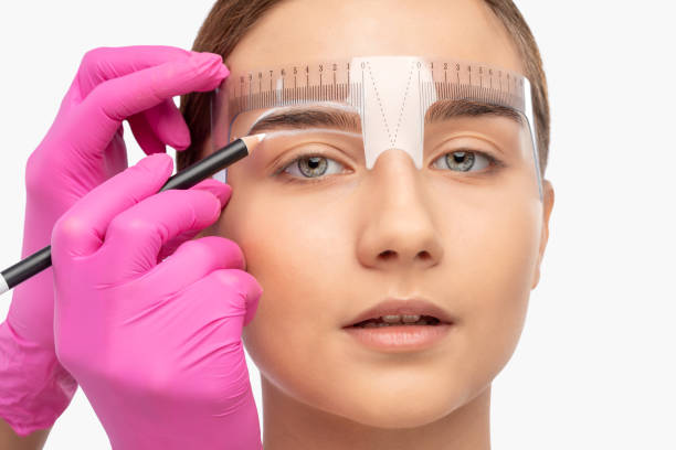 istock Make-up artist makes markings with white pencil for eyebrow and paints eyebrows. Professional makeup and facial care. 1299793728