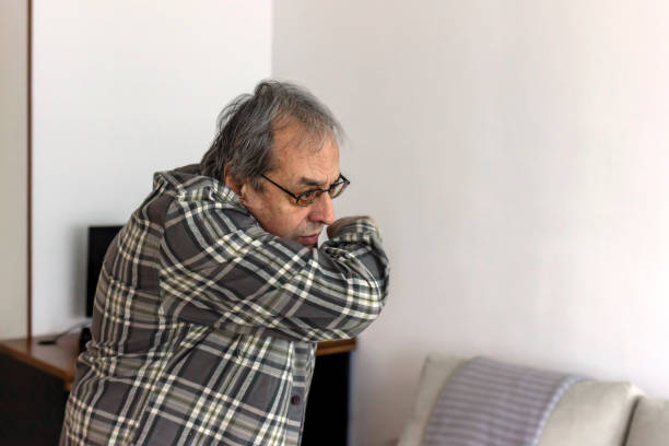 Frustrated elderly man sneezing and coughing into elbow.