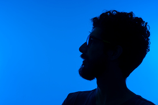 Young man looking up portrait silhouette in studio isolated on blue background.