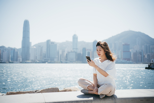 Asian cheerful young woman using her smartphone by the promenade.