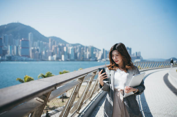 istock Asian cheerful young woman using her smartphone by the promenade 1299798426