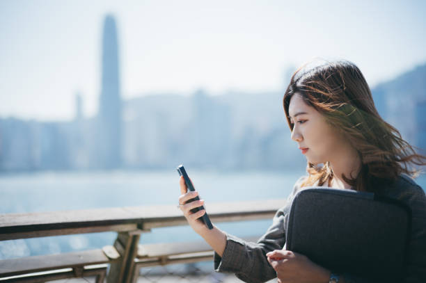 istock Asian cheerful young woman using her smartphone by the promenade 1299798449