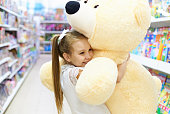 Little happy girl hugs a huge stuffed teddy bear in a toy store.