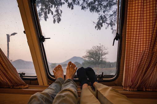 Legs of young couple relaxing in camper van with mountain view on lakeside in the morning