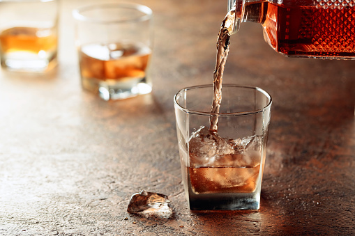 Pouring whiskey in glass with ice. Dammed glass with strong alcoholic drink.