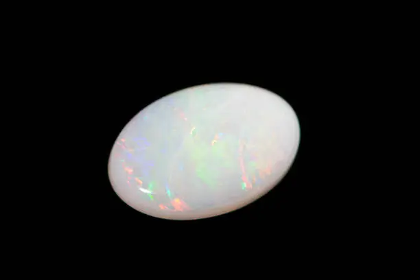White oval opal isolated on black background. Close-up.