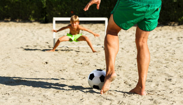 papa hat spaß mit seinem sohn spielen mit einem fußball am strand, im sommer an einem sonnigen tag. - military training camp stock-fotos und bilder