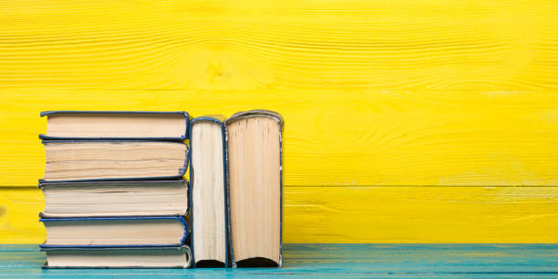 istock Books on bookshelf in Library. Back to School education concept on colored abstract yellow background. Open hardback book stack in a raw on wooden desk table. 1299804053