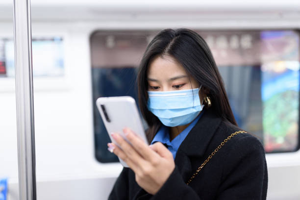 istock Young Asian woman wearing protective mask and using smart phone in subway train.Mode of transport during COVID-19 pandemic. 1299804643